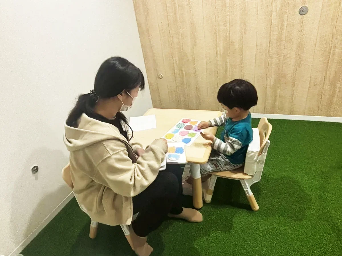 室内の芝生エリアで、机をはさんで子どもと一緒に課題に取り組むスタッフ