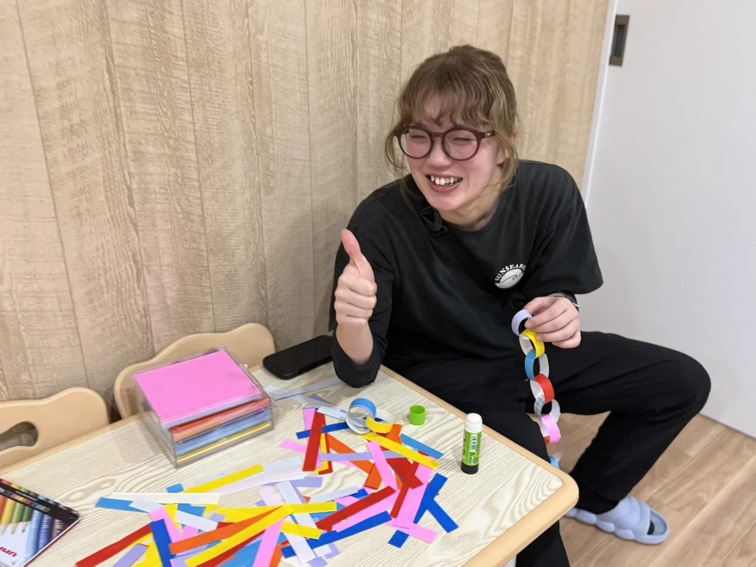 色紙で輪飾りを作りながら、笑顔で親指を立てる採用担当のスタッフ