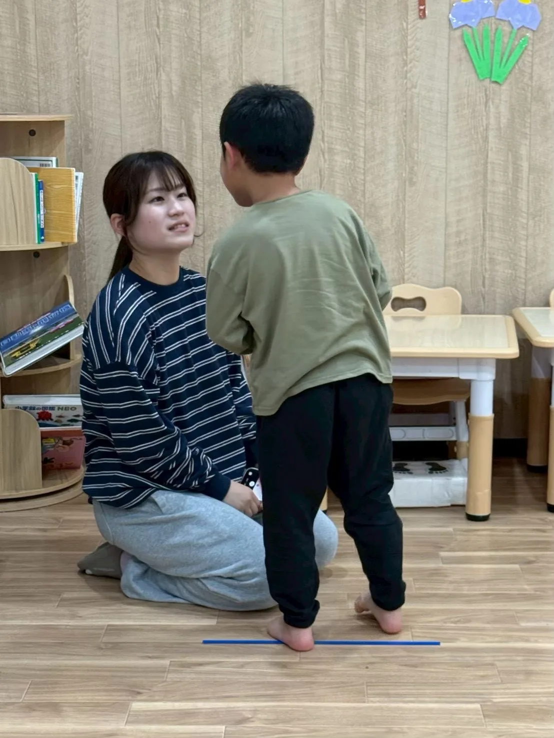 教室の床に座り、立っている子どもと目線を合わせて話すスタッフ