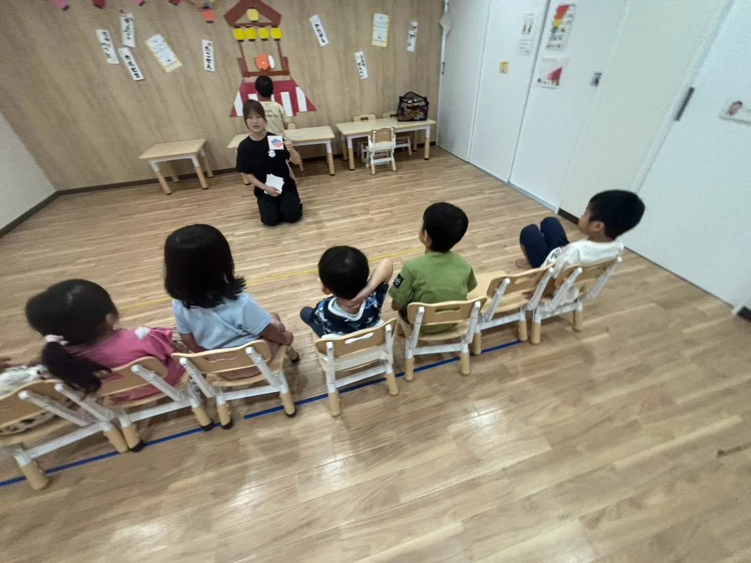 椅子に並んで座る子どもたちの前で、カードを見せながら集団活動を進行するスタッフ