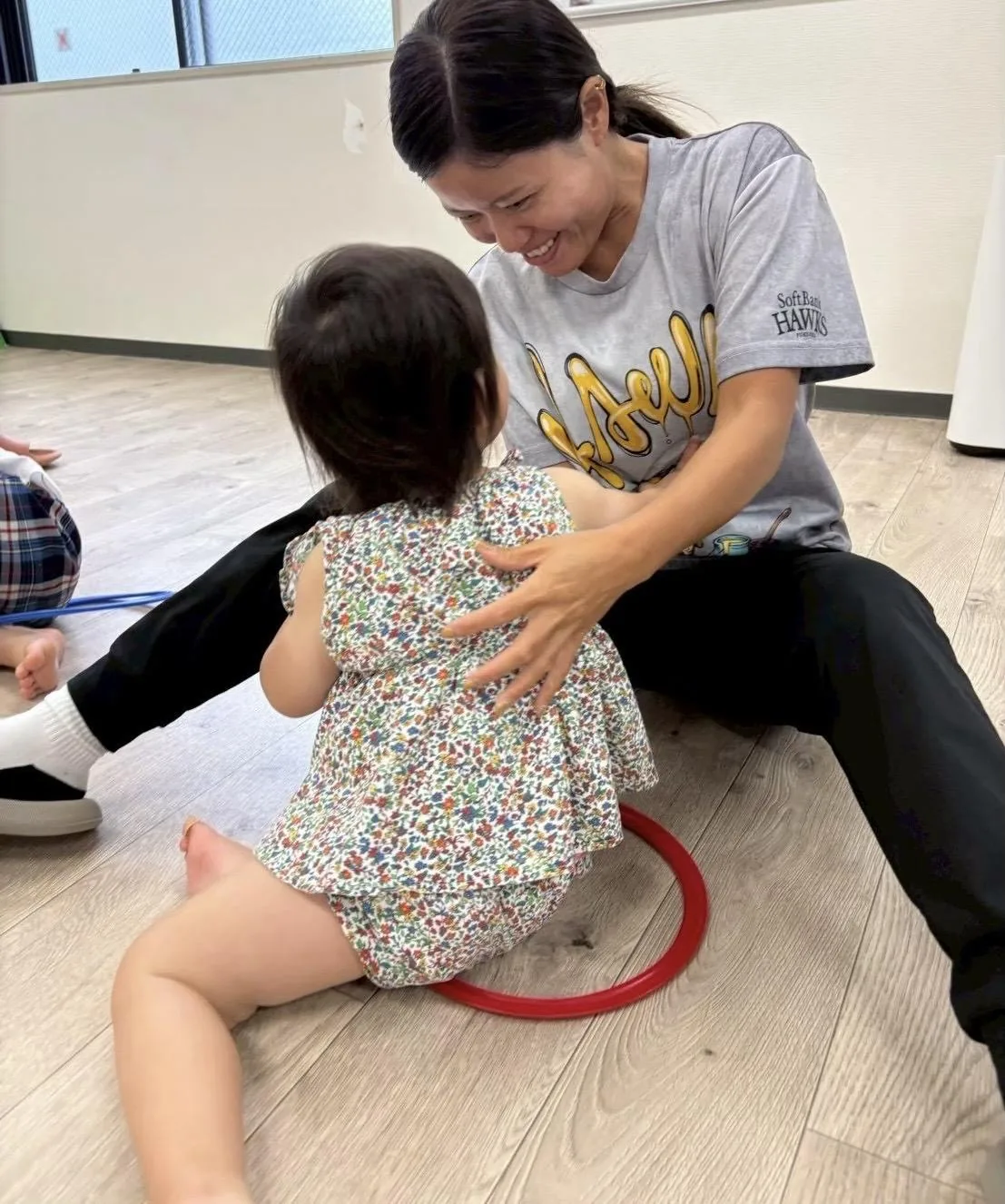 床に座って小さな子どもを抱きとめ、笑顔で関わるスタッフ